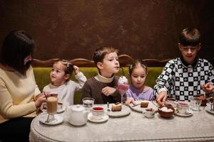 famille heureuse mangeant des desserts ensemble dans un café confortable et s'amusant. garçon enfant boire du lait frappé. photo