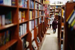 petites soeurs en veste atteignant un livre de la bibliothèque à la bibliothèque. l'apprentissage et l'éducation des enfants européens. photo