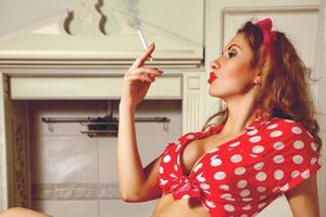 jolie jeune femme aux cheveux bouclés fumant une cigarette dans la cuisine photo