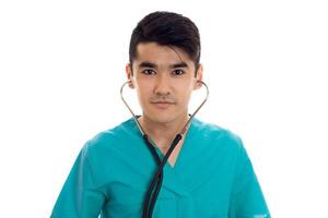 Closeup portrait of young beautiful brunette man doctor in blue uniform with stethoscope looking at the camera isolated on white background photo