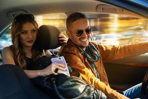 un homme à la mode souriant conduit à toute vitesse avec une superbe fille sur le siège arrière et un sac plein d'argent au milieu photo