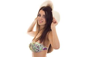 jeune femme brune mignonne aux gros seins naturels en maillot de bain avec motif floral et chapeau de paille souriant et regardant la caméra isolée sur fond blanc photo