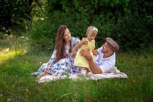 une jeune famille heureuse joue avec leur petite fille au pré vert photo