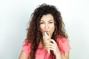 amusante jeune fille aux cheveux bouclés mange de la glace photo