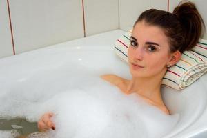 jolie jeune fille se trouve dans un bain à remous avec de la mousse et se penche sur la caméra photo