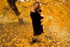 jeune fille en manteau noir à l'extérieur dans les feuilles d'automne photo