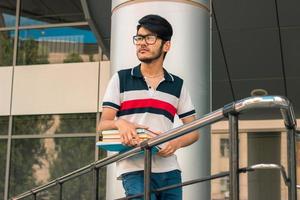 élégant jeune homme à lunettes debout dans la rue avec des livres photo