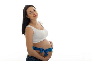 une jeune femme enceinte se tient sur le côté avec un ruban sur le ventre isolé sur fond blanc photo