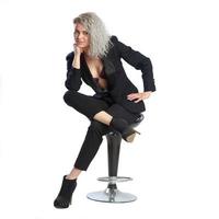 femme aux cheveux bouclés blonds en costume noir est assise sur une chaise photo