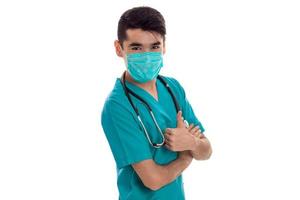 Bel homme médecin posant en uniforme et masque isolé sur fond blanc en studio photo