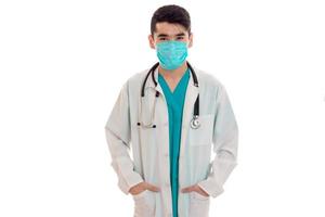mignon médecin élégant en uniforme bleu avec stéthoscope et masque posant et regardant la caméra isolée sur fond blanc photo