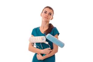 Jeune femme brune fatiguée constructeur en uniforme avec un rouleau à peinture dans les mains faire des rénovations isolées sur fond blanc photo