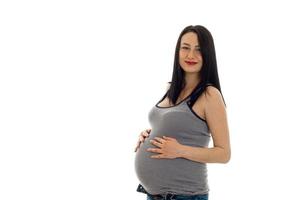 jeune fille enceinte aux cheveux noirs touchant son gros ventre et regardant la caméra isolée sur fond blanc photo