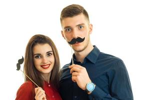 une jeune fille et un gars joyeux tiennent une moustache en papier photo