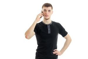 un charmant jeune homme vêtu d'un t-shirt noir a l'air droit et garde un téléphone portable près de votre oreille photo