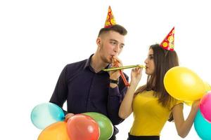 un gars et une fille drôles se tiennent l'un en face de l'autre, soufflent des cornes et transportent des ballons multicolores photo