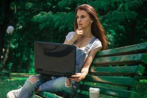 jeune fille charmante est assise sur un banc et utilise un ordinateur portable photo