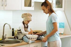 jolie petite fille homecook avec sa belle mère fait des crêpes dans la cuisine blanche. photo