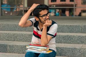 portrait d'un jeune homme mignon à lunettes qui est assis dans une rue avec des livres photo