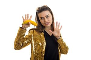 jolie brune élégante en veste dorée avec une banane dans les mains photo