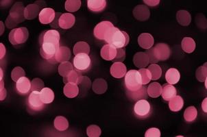 lumières colorées festives floues sur fond noir utiles comme arrière-plan. image tonique en viva magenta, couleur de l'année 2023 photo
