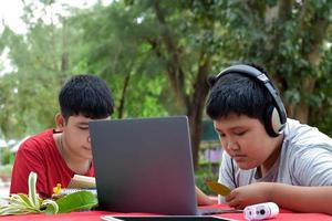 les jeunes garçons asiatiques font leurs devoirs et font les rapports sur diverses espèces de forêts tropicales en utilisant des ordinateurs portables, des loupes, des cahiers, des jumelles de poche et des tablettes, un concept d'ordinateur portable maquette. photo