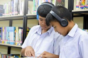 soft fucus de deux étudiants asiatiques écoute les médias, lit et consulte le livre préféré à la bibliothèque de l'école photo