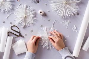 les mains des enfants collent une perle à un flocon de neige en papier sur fond gris. décor fait à la main. vue de dessus. photo