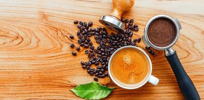 vue de dessus de la tasse à café expresso et de l'équipement de l'outil de café barista porte-filtre avec tamper et grains de café torréfiés foncés avec feuille de café vert sur table en bois photo