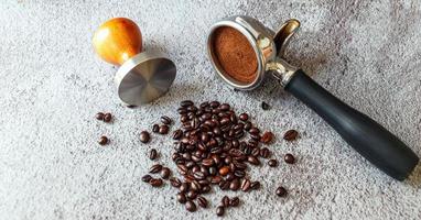 équipement dans un café de café barista outil porte-filtre avec tamper et grains de café torréfiés foncés sur fond gris photo