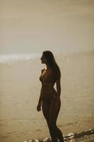 jeune femme en bikini marchant au bord de la mer sur un coucher de soleil de jour d'été photo