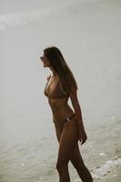 jeune femme en bikini marchant au bord de la mer sur un coucher de soleil de jour d'été photo