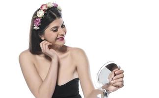 belle femme brune séduisante vérifiant la peau de son visage devant un miroir sur fond blanc photo