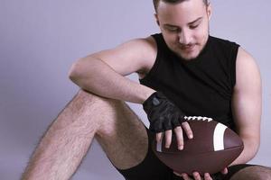 jeune bel homme américain tenant un ballon de rugby sur fond gris isolé photo