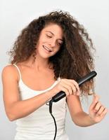 Belle fille aux cheveux ondulés irritée et attrayante fer à lisser les boucles désordonnées traitement de thérapie à la kératine photo