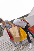 portrait d'un jeune couple caucasien joyeux homme et femme tenant de nombreux sacs en papier après avoir fait du shopping en marchant et en parlant dans la rue. couple de famille heureux avec forfaits en plein air. notion d'achat photo