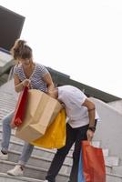 portrait d'un jeune couple caucasien joyeux homme et femme tenant de nombreux sacs en papier après avoir fait du shopping en marchant et en parlant dans la rue. couple de famille heureux avec forfaits en plein air. notion d'achat photo