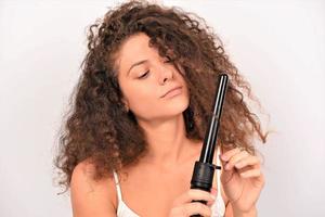 belle femme souriante aux longs cheveux ondulés le repassant, à l'aide d'un fer à friser. fille heureuse avec de magnifiques cheveux lisses et sains utilisant un bigoudi pour des boucles parfaites. coiffure et coiffure photo