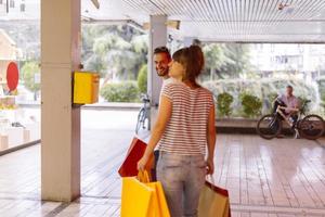 portrait d'un jeune couple caucasien joyeux homme et femme tenant de nombreux sacs en papier après avoir fait du shopping en marchant et en parlant dans la rue. couple de famille heureux avec forfaits en plein air. notion d'achat photo