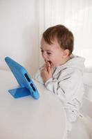 heureux petit garçon jouant au jeu sur tablette numérique à la maison. portrait d'un enfant à la maison regardant un dessin animé sur la tablette. technologie moderne pour les enfants et l'éducation. photo