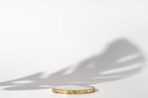podium en marbre avec or sur fond blanc avec ombre de plante tropicale. podium pour produit, présentation cosmétique. maquette créative. piédestal ou plate-forme pour produits de beauté. photo