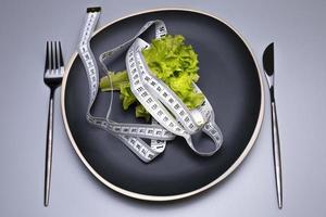 salade verte et ruban à mesurer dans l'assiette. la notion de régime. photo