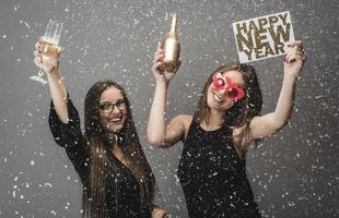 deux amies célébrant le nouvel an avec des confettis et du champagne tenant une pancarte. isolée photo
