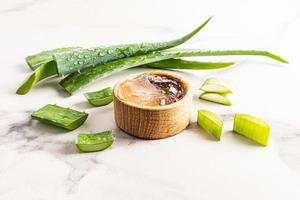 bol en bois avec gel cosmétique bio aloe vera sur fond blanc marbré parmi les tranches de la plante. cosmétiques naturels. photo