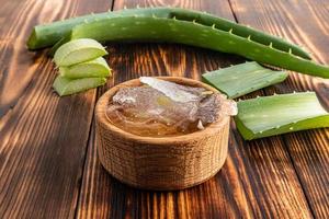 une coupe de la pulpe d'aloe vera dans un bol en bois sur une table de village parmi les feuilles . vue de face. le concept de préparation du gel à la maison. photo