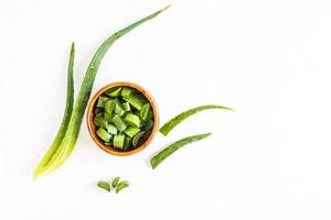 vue de dessus d'un bol en bois avec des tranches de la plante d'aloe vera et des feuilles sur fond blanc. style plat. plante médicinale. alternative à la médecine photo