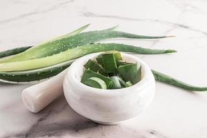 un mortier en marbre blanc avec un pilon avec des tranches d'aloe vera tranchées sur un fond de marbre à côté des feuilles fraîches de la plante. fond de marbre. photo