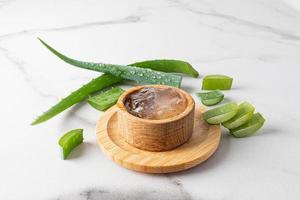 gel d'aloe vera dans un bol en bois sur fond de marbre avec des feuilles et des tranches d'aloès frais. le concept de soins de la peau du visage, du corps, des cheveux. photo