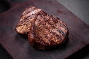 Délicieux steak de boeuf juteux frais avec des épices et des herbes sur un fond de béton foncé photo