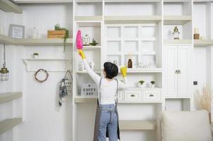 jeune femme asiatique heureuse balayant le canapé et les meubles pour nettoyer la maison, concept de mode de vie sain photo